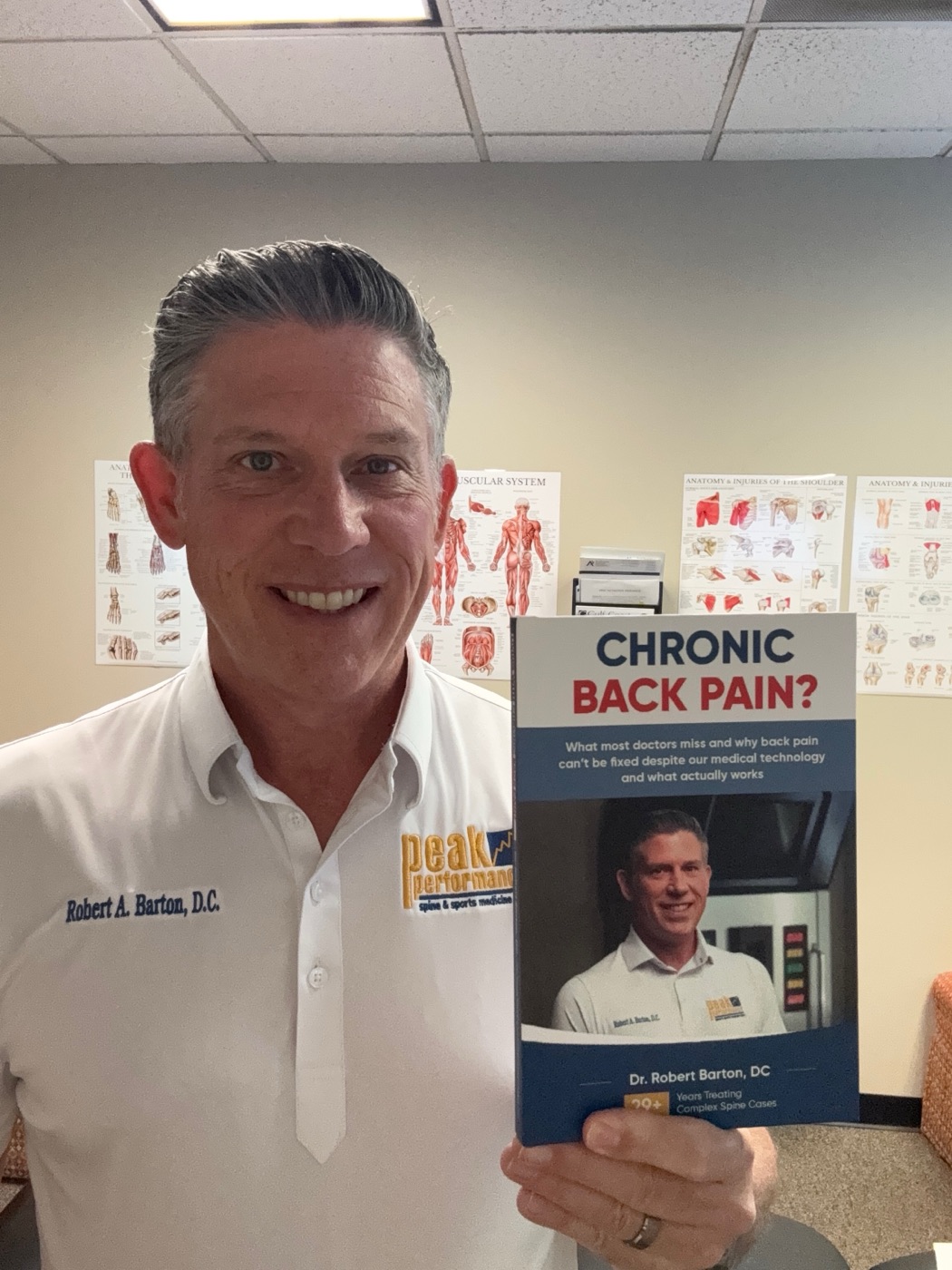 Dr. Barton holding his book, Chronic Back Pain?, in the clinic